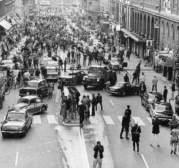a black and white photo of a crowded city street filled with vintage cars and pedestrians, with a military vehicle in the…