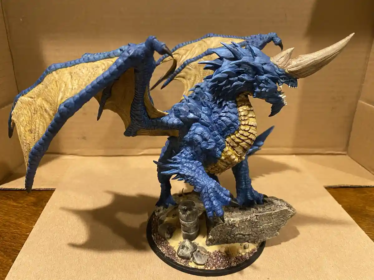 A detailed blue and gold dragon figurine with large wings, a horn, and spiked scales stands on a rocky base inside a…