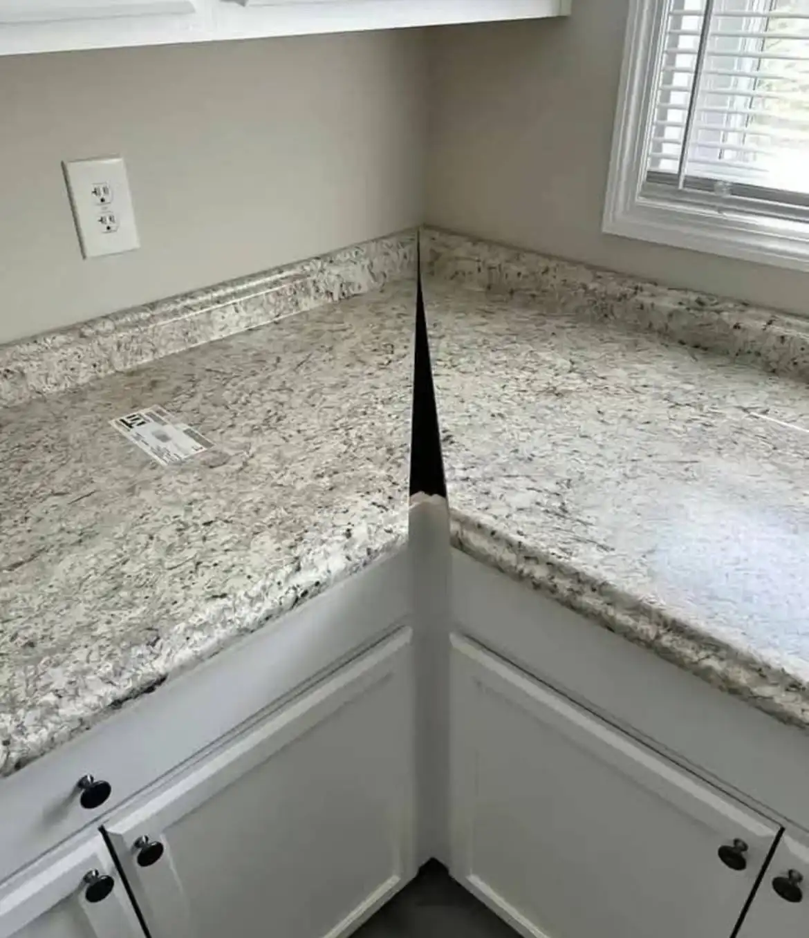 A kitchen countertop corner where the granite surface appears to split into two planes, revealing a black pencil-like object…