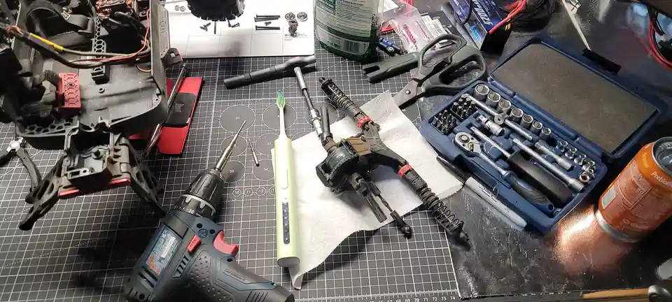 A cluttered workbench displays a disassembled drone, a drill, a socket set, and other tools, with a toothbrush placed…