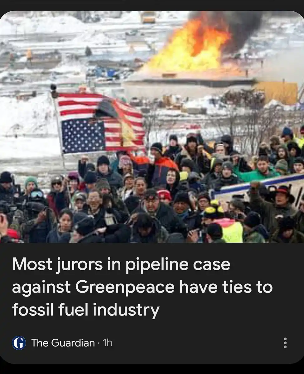 A snowy protest scene with a large crowd of people, some holding an American flag, while a large fire burns in the…