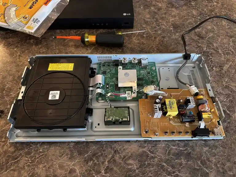 An overhead shot of an open electronic device, likely a TV or set-top box, revealing its internal circuit boards, fan, and…