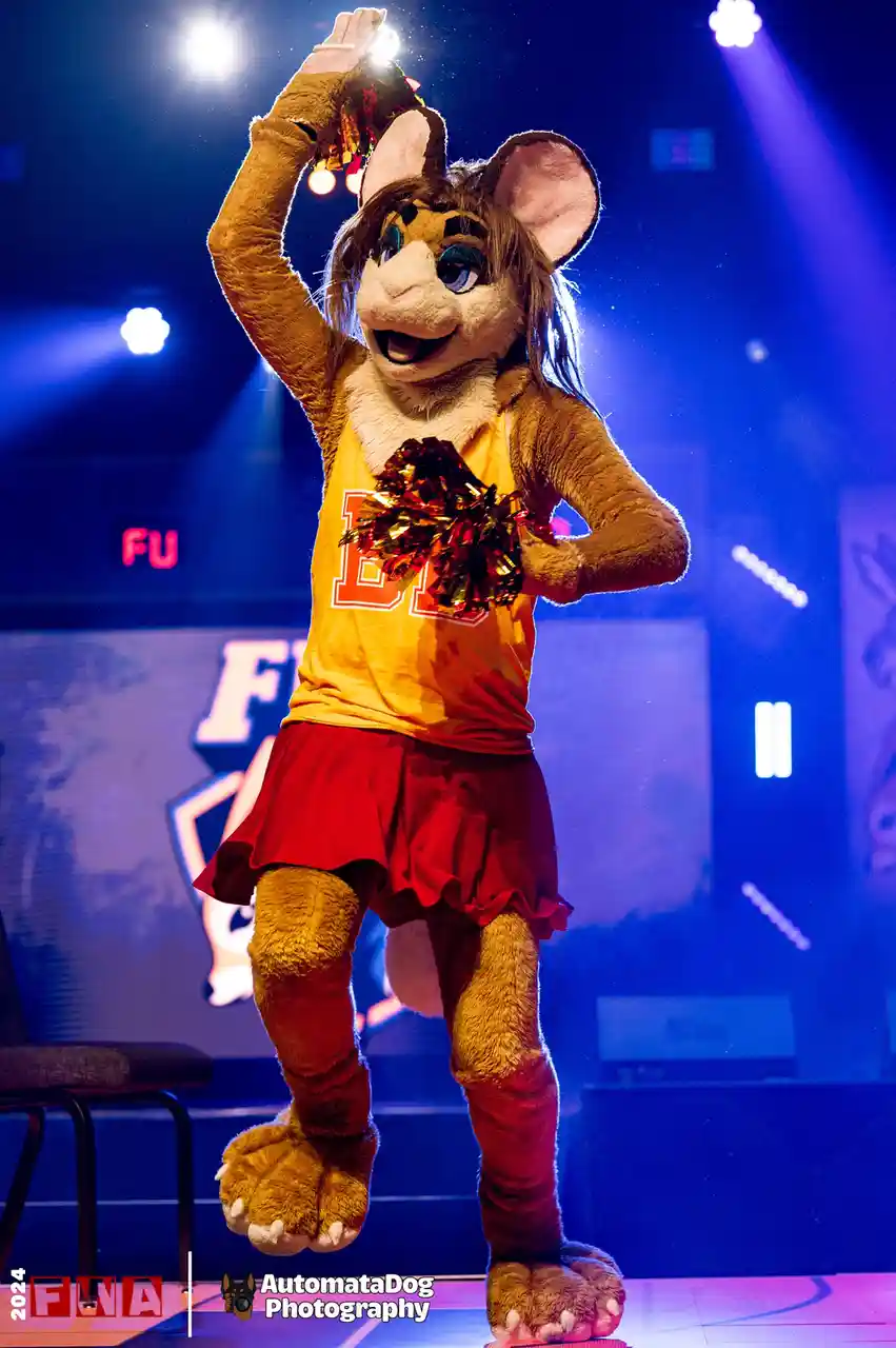 A person in a detailed brown fursuit of a cheetah-like anthropomorphic animal, wearing a yellow tank top with a large red…