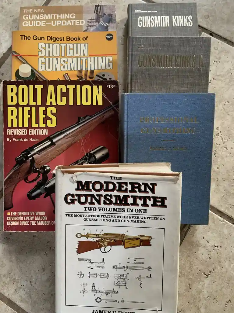 A collection of six gunsmithing books is arranged on a tiled floor, including titles like 'Gunsmith Kinks', 'Bolt Action…