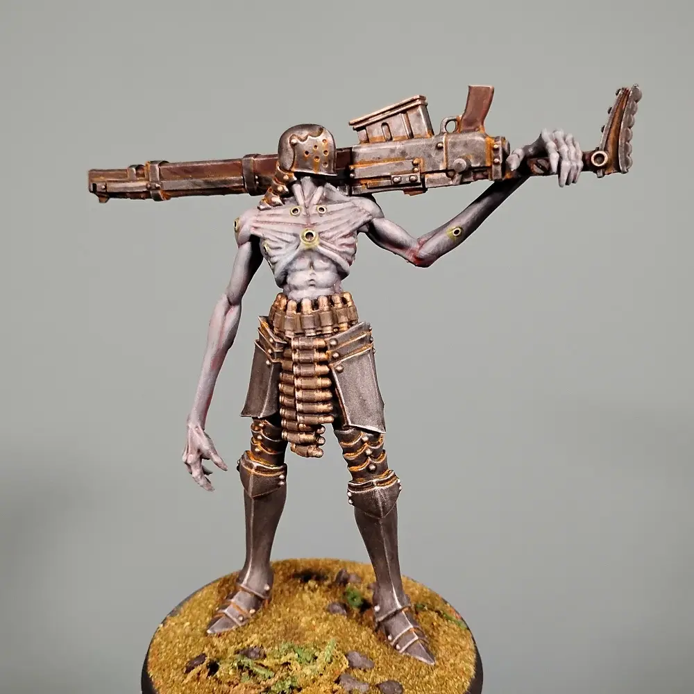 A painted miniature figurine of a humanoid skeleton wearing armor and carrying a large machine gun slung over its shoulder…