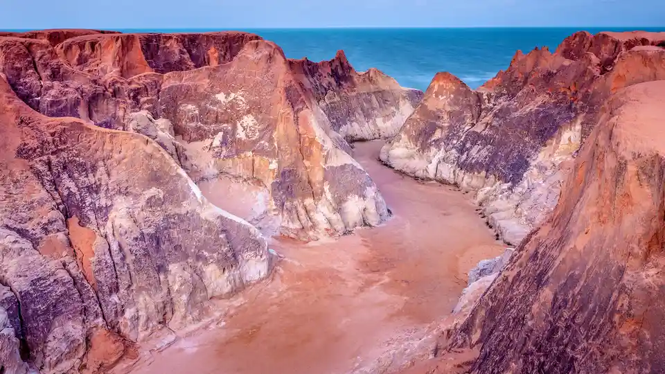 Breathtaking yet vulnerable, Morro Branco beach's reddish cliffs meet the Atlantic waves. Wind, rain, and erosion…