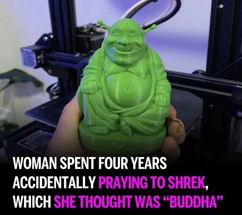 A hand holds a green 3D-printed figurine of Shrek sitting cross-legged like a Buddha, in front of a 3D printer. The overlaid…