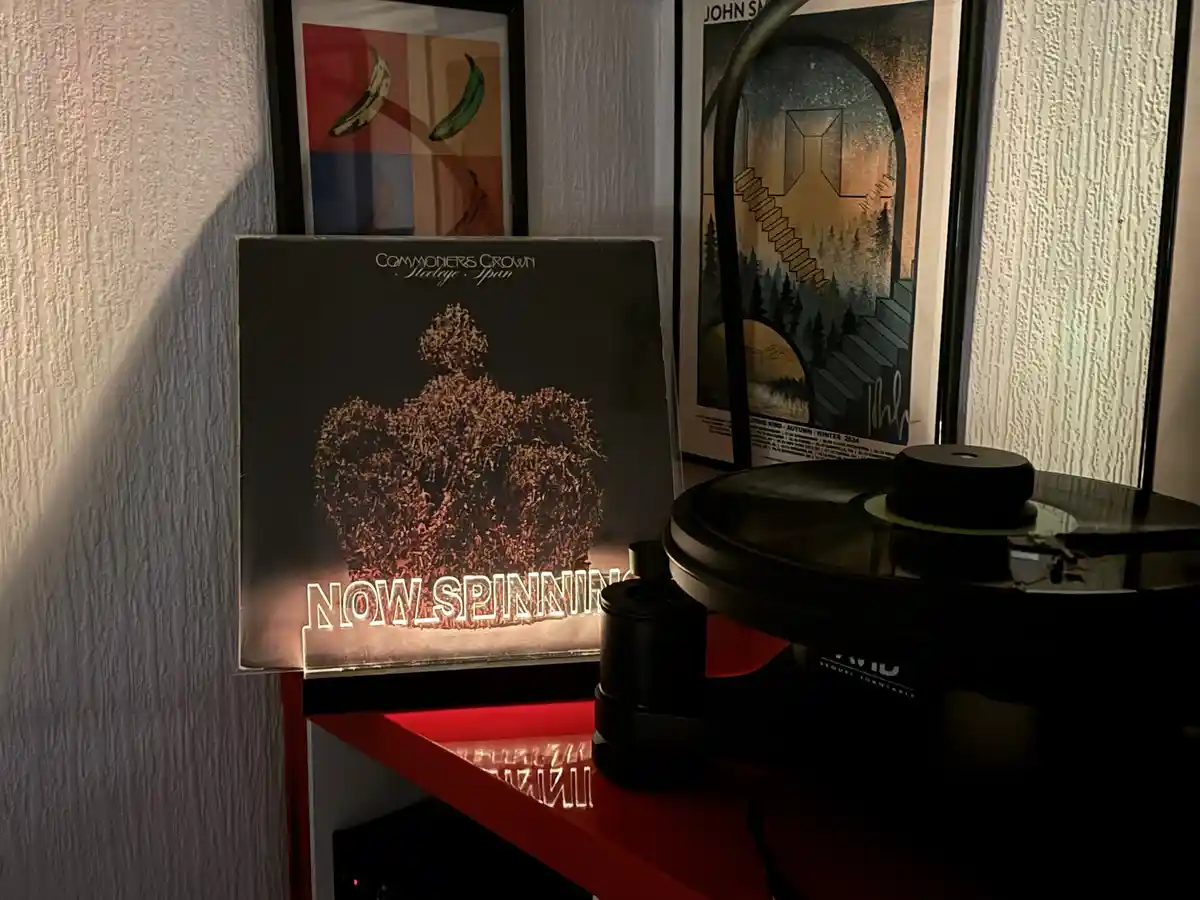 A vinyl record player sits on a red shelf with the album 'Commoners Crown' by Steeleye Span standing upright beside it. The…