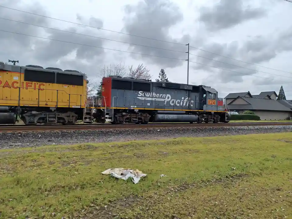 A photograph of two Southern Pacific locomotives on railway tracks under a cloudy sky, with a pile of trash in the…