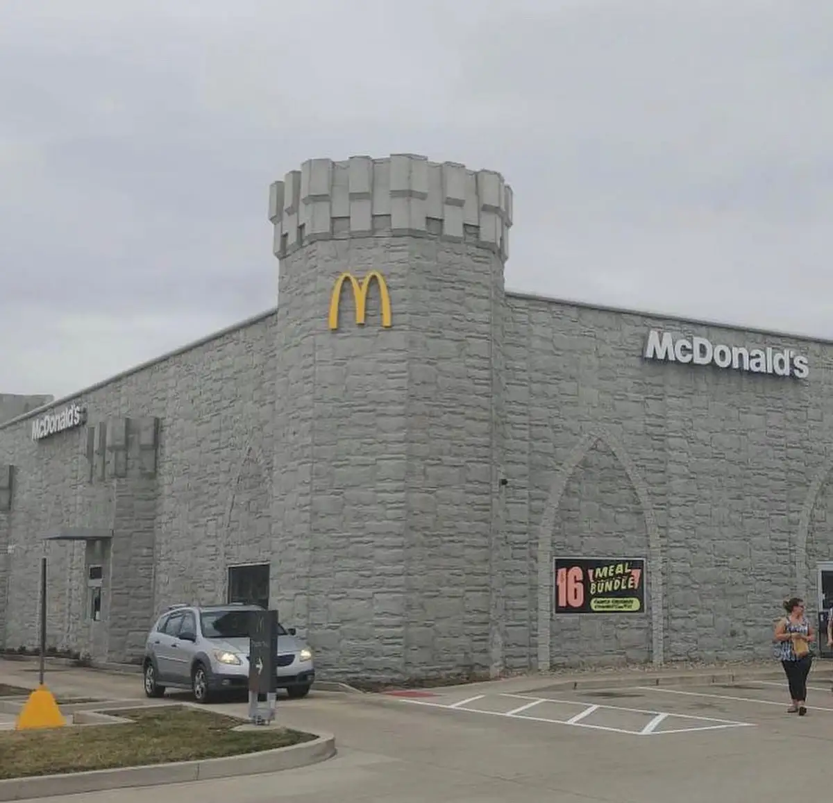 An exterior shot of a McDonald's restaurant with a gray stone facade and a castle-like tower, featuring the yellow…