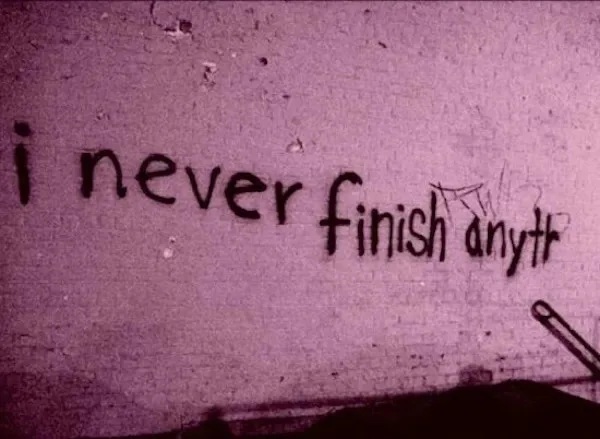 A close-up of rough, textured wall with handwritten text in black marker that reads 'i never finish anytr', with the word…