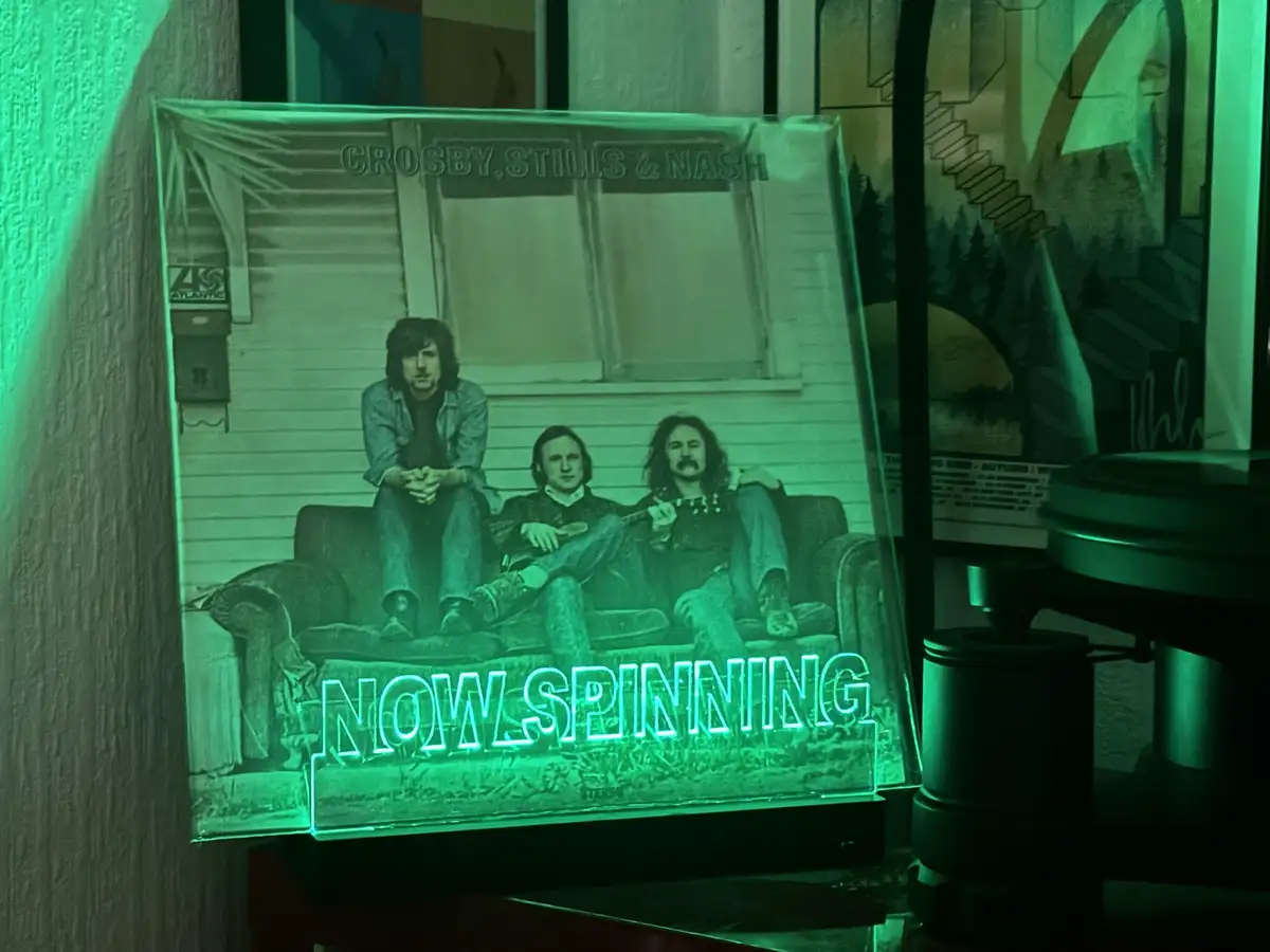 A green-tinted 3D LED lamp displays the cover art of the Crosby, Stills & Nash album, showing the three musicians sitting on…