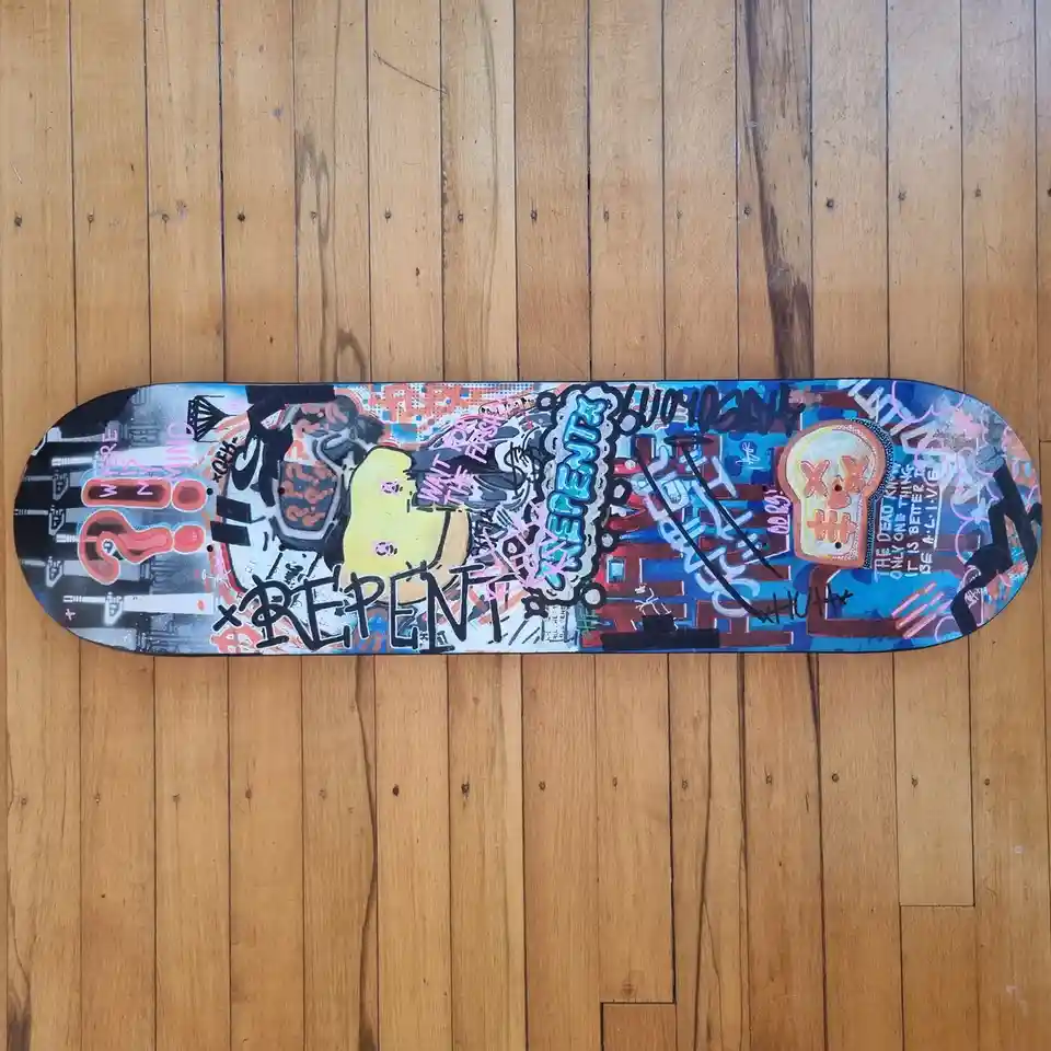 A skateboard deck covered in colorful graffiti art, featuring a yellow cartoon character, question marks, and various…