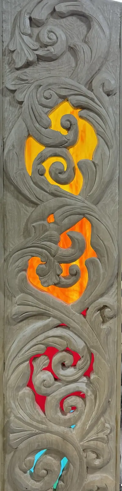 A vertically oriented wooden panel with intricate, swirling carvings that form three distinct cutouts. Through each cutout…
