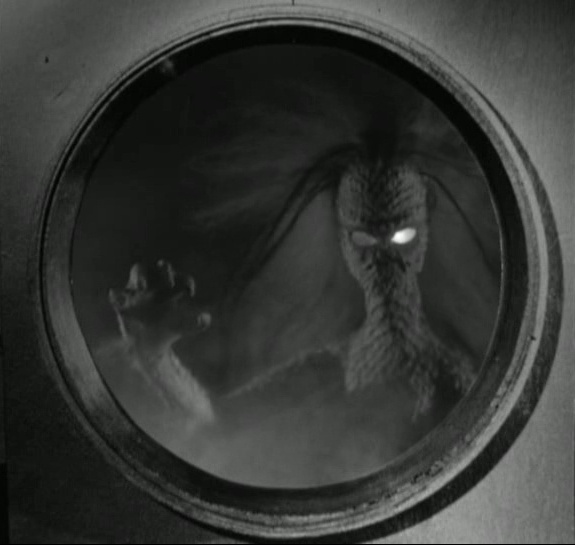 A black-and-white still from a classic monster movie shows a large, scaly, reptilian creature with glowing eyes peering…