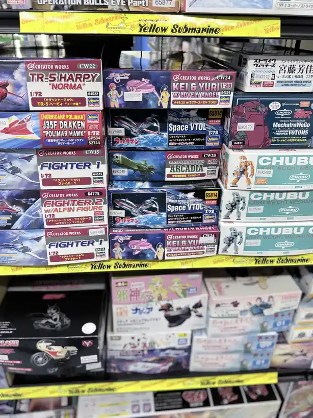 A store shelf filled with various Japanese model kits, including spaceships, mechs, and anime-themed figures, with visible…