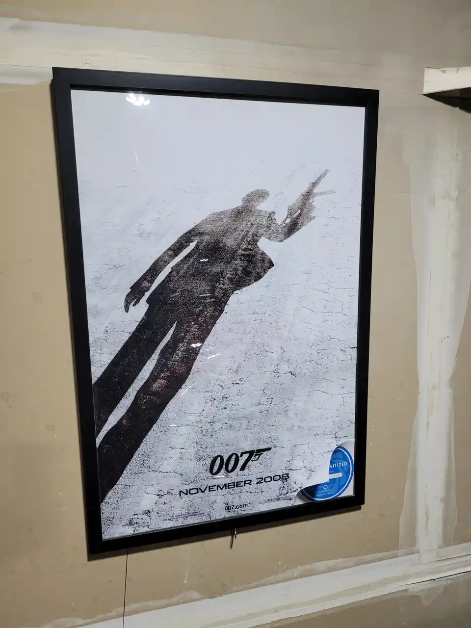 A framed, black-and-white James Bond movie poster featuring a silhouetted figure in a suit holding a gun, mounted on a wall…