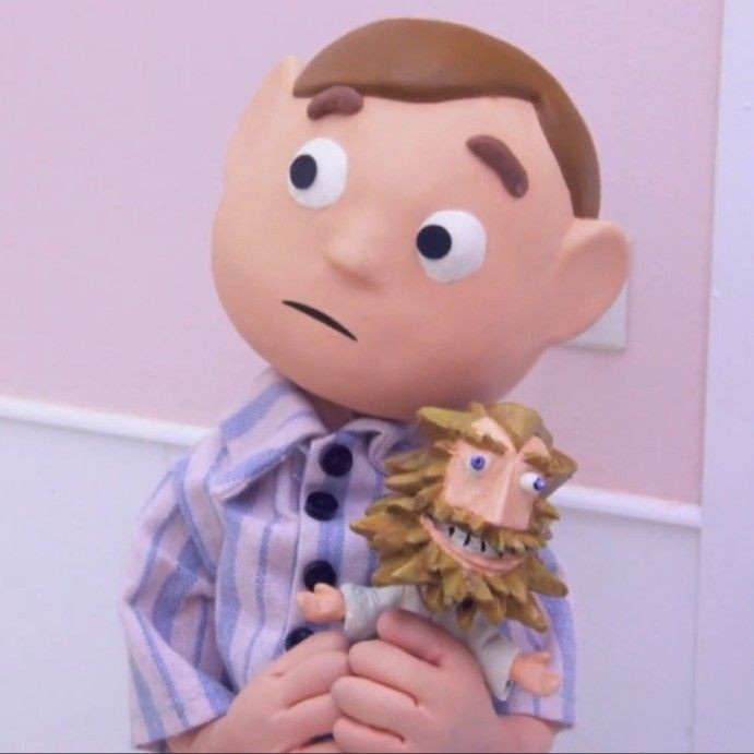 A claymation character with large eyes and a worried expression holds a smaller, bearded puppet with a grinning, mischievous…