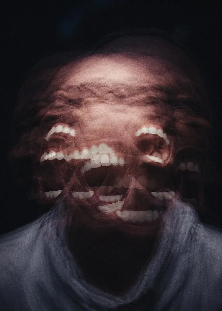 A distorted, blurry image of a person's face with multiple overlapping mouths open in wide, toothy grins against a dark…