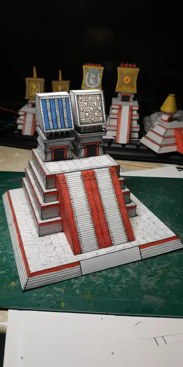 A handmade paper model of a stepped pyramid, resembling an ancient Mesoamerican structure, is constructed from stacked books…