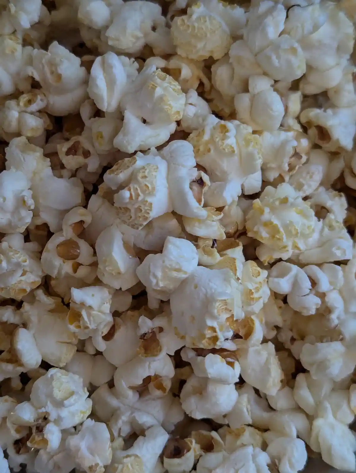 A close-up photo shows a pile of white, fluffy popcorn with some kernels still partially intact and showing their brownish…