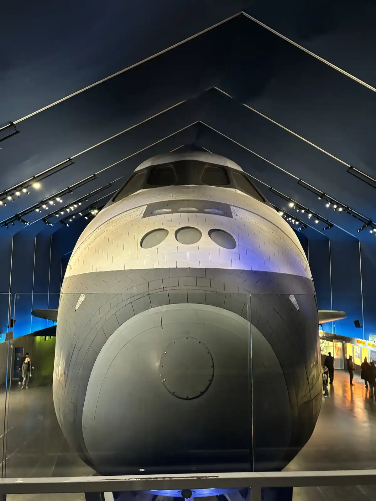 A close-up shot of the front of the Space Shuttle Enterprise on display in a museum, with its cockpit windows and three…