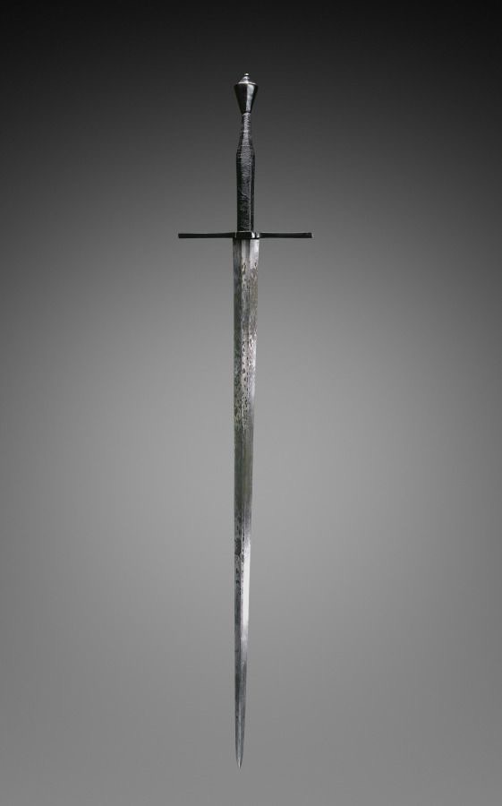A vertically oriented, ornate medieval-style sword with a textured grip, crossguard, and pointed tip, displayed against a…