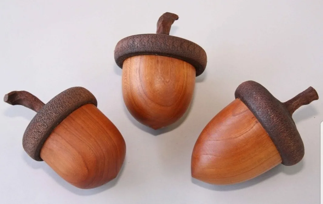 Three hand-carved wooden acorns with detailed caps and stems are arranged on a plain white surface. The overlaid text reads…