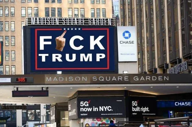 A large digital billboard at Madison Square Garden displays the text 'F**K TRUMP' in bold white letters on a dark blue…