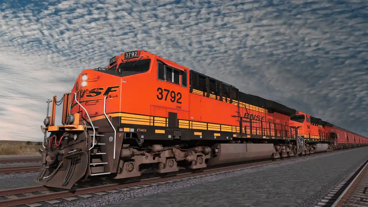 A bright orange BNSF freight train, led by locomotive number 3792, travels along tracks under a cloudy sky. The overlaid…
