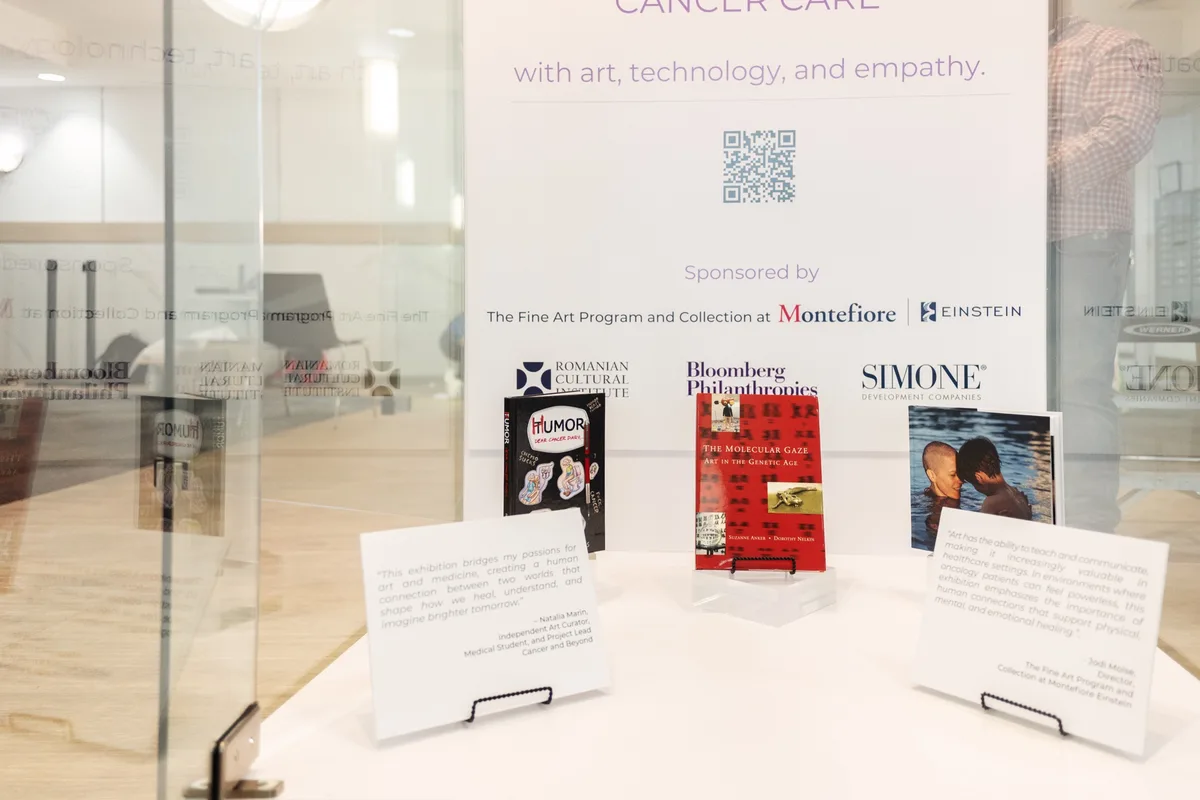 A display case at a cancer care exhibition features books and quotes about art and medicine, with a book titled 'HUMOR'…