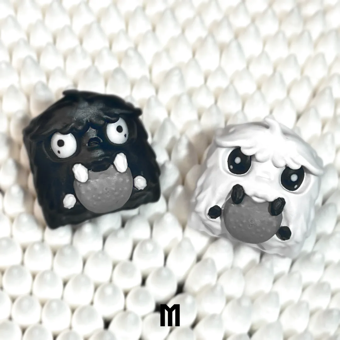 Two small, handmade clay figures—one black and one white—sit side by side on a bed of white cotton swabs. Both have large…