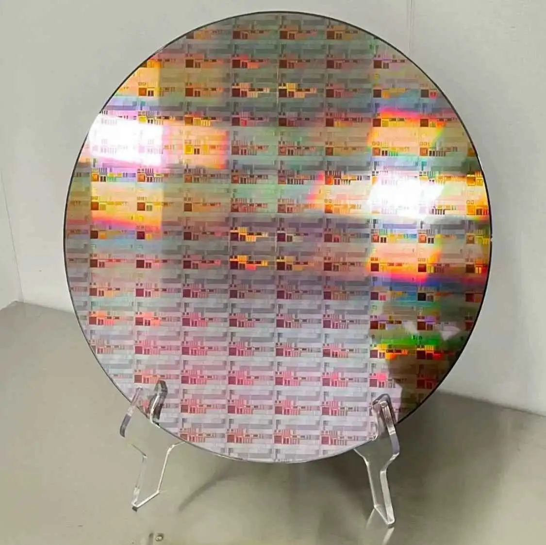 A circular silicon wafer with a grid of microchips, displaying iridescent rainbow reflections from light, is mounted on…