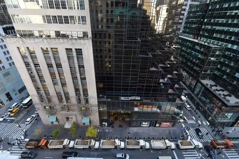 An aerial view of Trump Tower in New York City, showing its distinctive glass facade next to a beige building, with a row of…