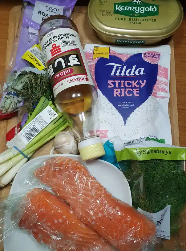 A wooden cutting board displays various grocery items including salmon fillets, Tilda sticky rice, Mizkan sushi seasoning…