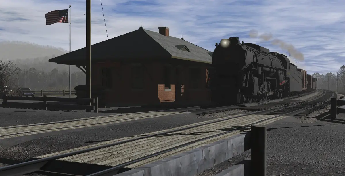 A steam locomotive pulls into a brick train station under a partly cloudy sky, with an American flag flying nearby. The…