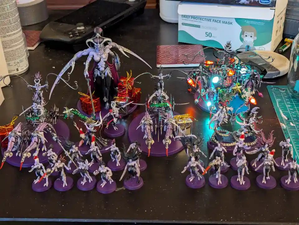 A collection of intricately painted fantasy miniatures, mostly dark-themed with purple bases, are arranged on a desk…
