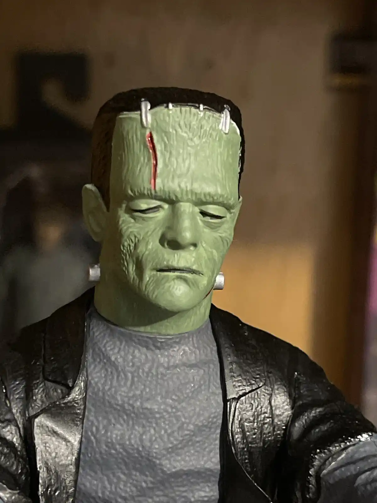 A close-up of a green Frankenstein's monster action figure with closed eyes, a red streak of blood running down its…