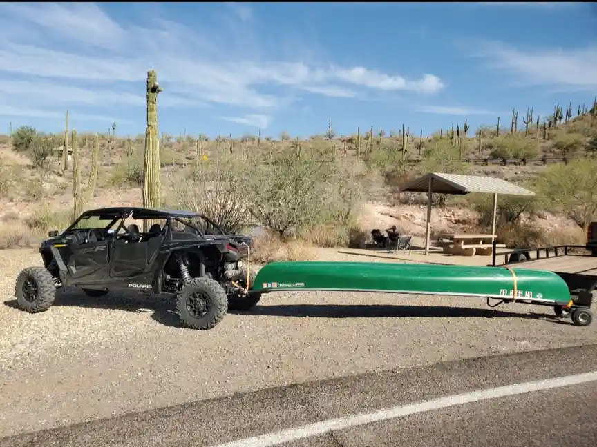 A black Polaris UTV is parked on a gravel shoulder next to a paved road in a desert landscape filled with saguaro cacti. The…