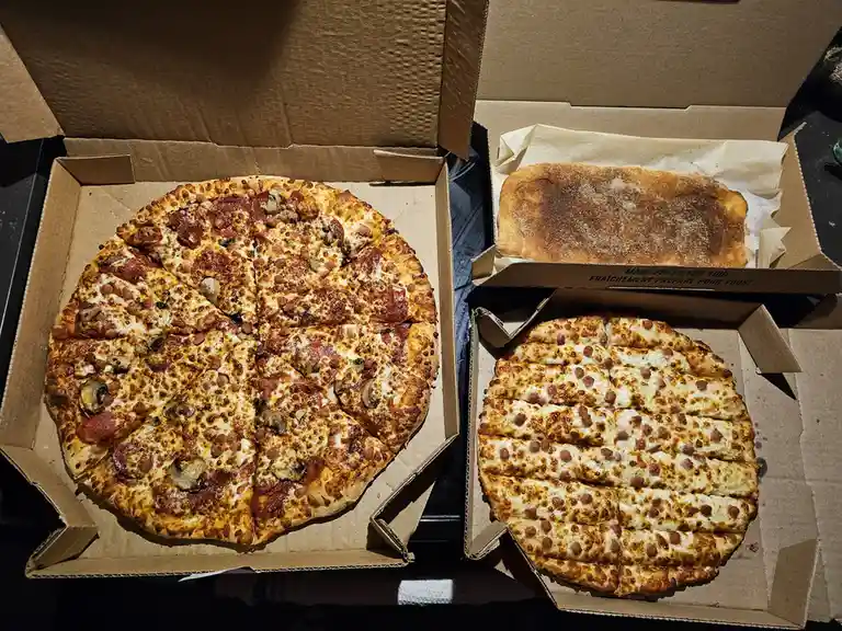 Two open cardboard pizza boxes sit side by side on a dark surface. The left box contains a round, sliced pepperoni and…