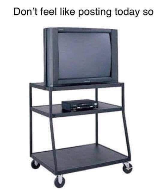 An old black CRT television sits on a three-tiered black metal cart with wheels. The middle shelf holds a small black…