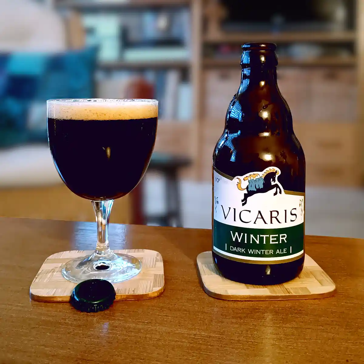 A dark winter ale bottle labeled 'VICARIS WINTER | DARK WINTER ALE |' sits next to a poured glass of the same dark beer with…