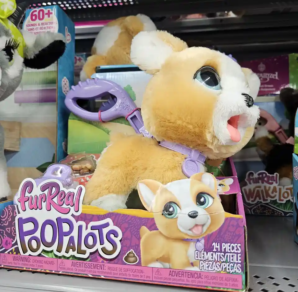 A FurReal 'Popalots' toy dog, with tan and white fur and large blue eyes, is displayed in its packaging on a store shelf…