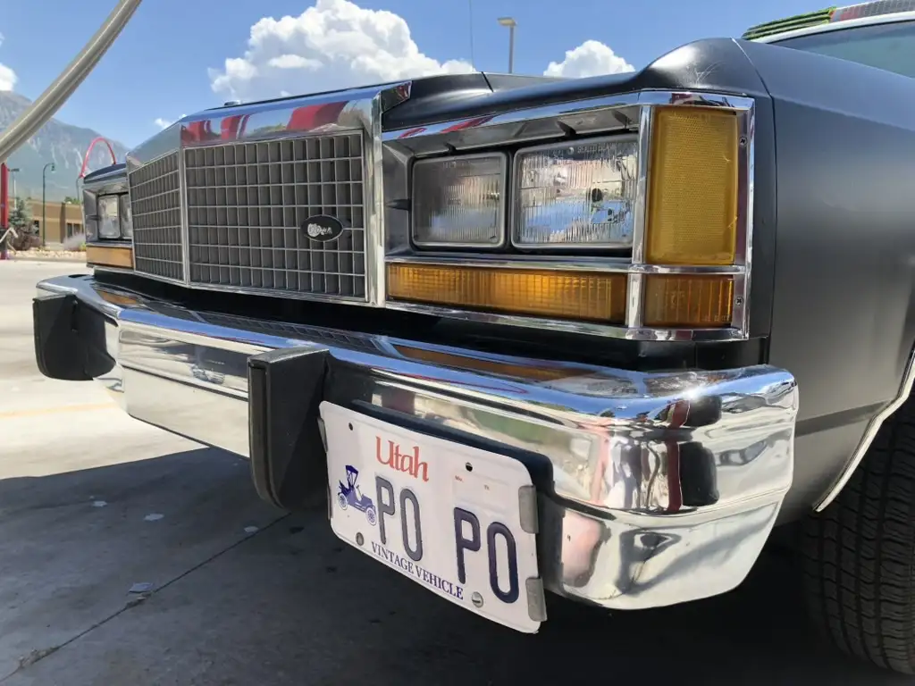 A close-up photo of the front bumper and grille of a vintage black Ford truck parked at a gas station, showing a Utah…