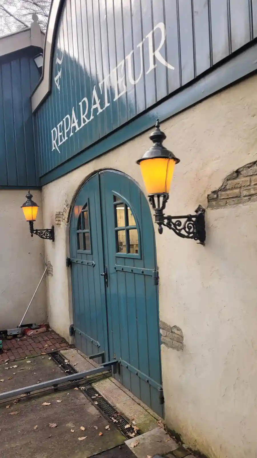 An exterior shot of a building with a teal arched door and matching teal siding, featuring the word 'REPARATEUR' in large…