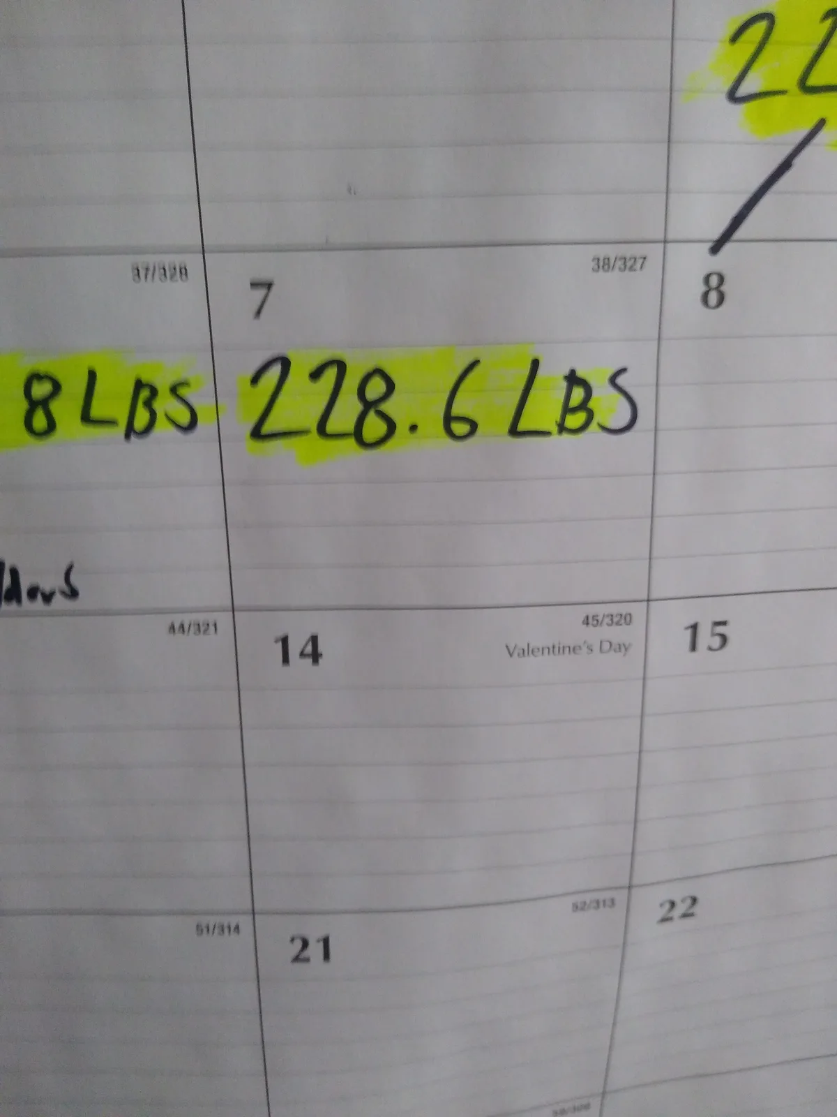 A close-up of a handwritten weight tracking log in a notebook, showing a weight of 228.6 LBS highlighted in yellow marker on…