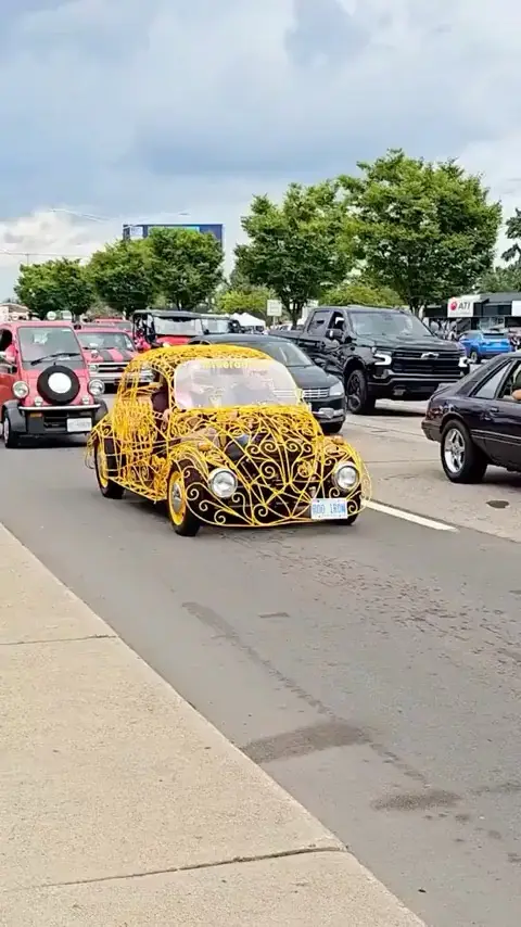 a vintage yellow volkswagen beetle is heavily decorated with an intricate, swirling yellow metal frame covering its body…