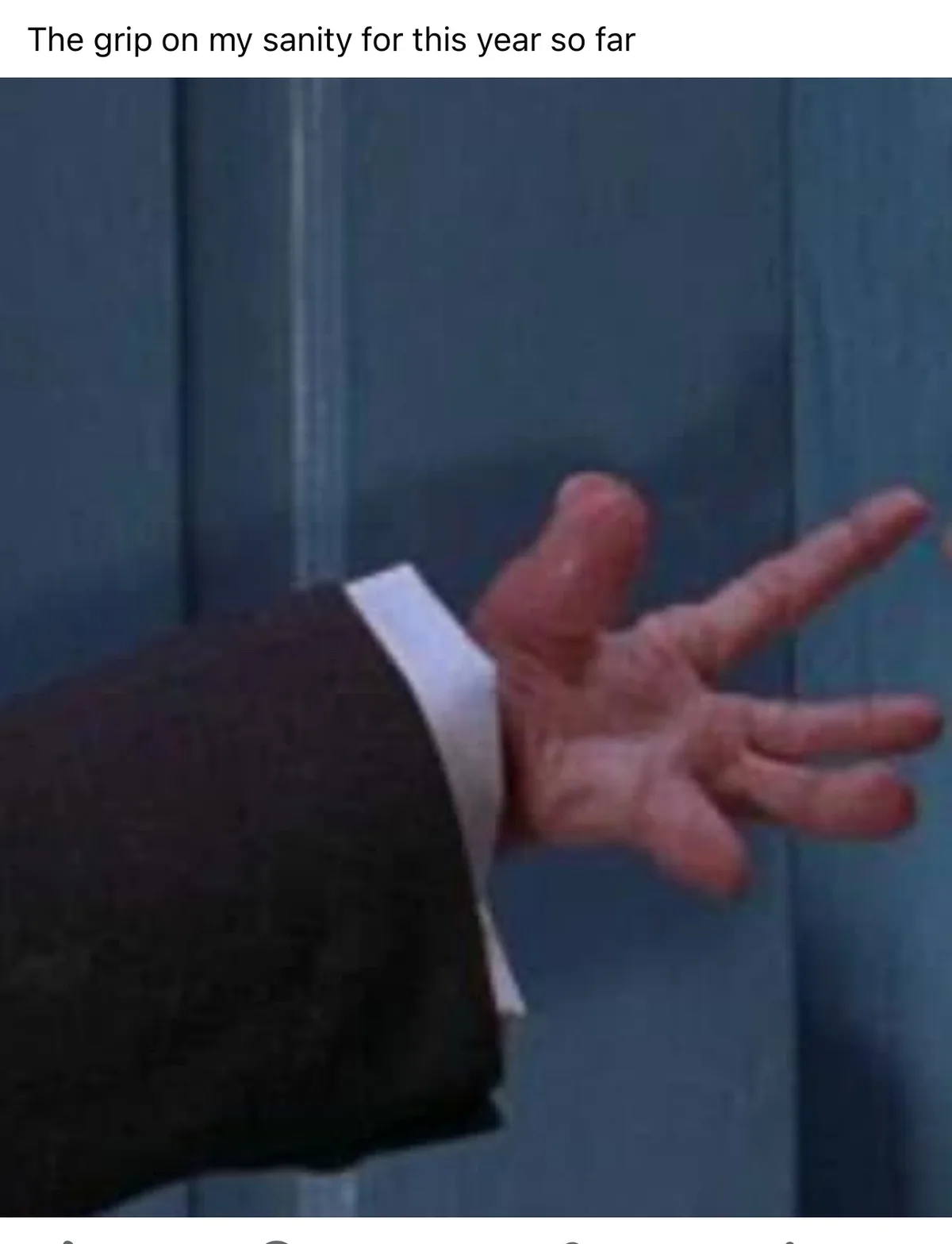 A close-up image shows a person's hand, wearing a dark suit jacket and white shirt cuff, gripping a blue door or wall with…
