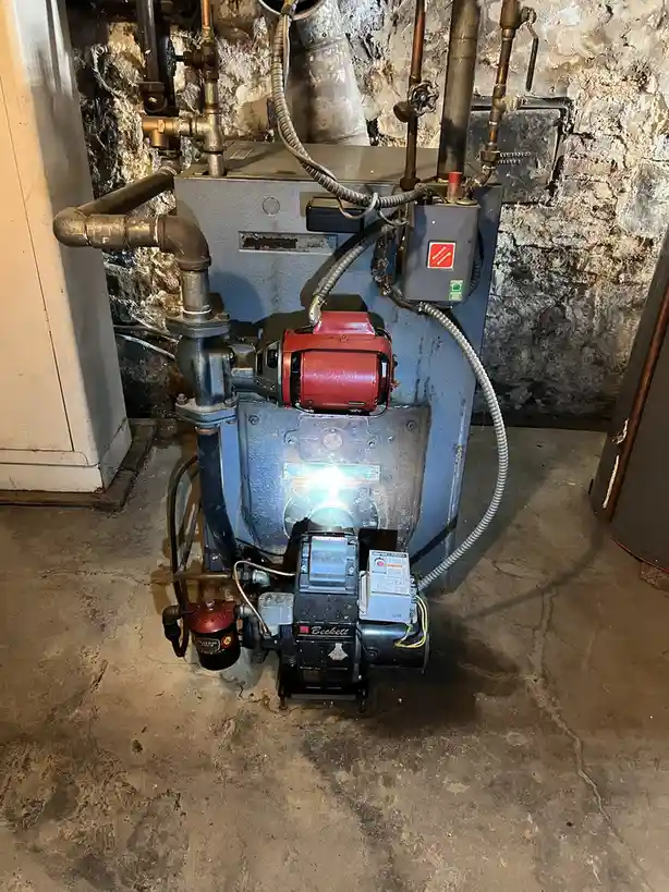 A close-up photo of an old, industrial-style boiler in a basement with exposed pipes and a stone wall, overlaid with the…