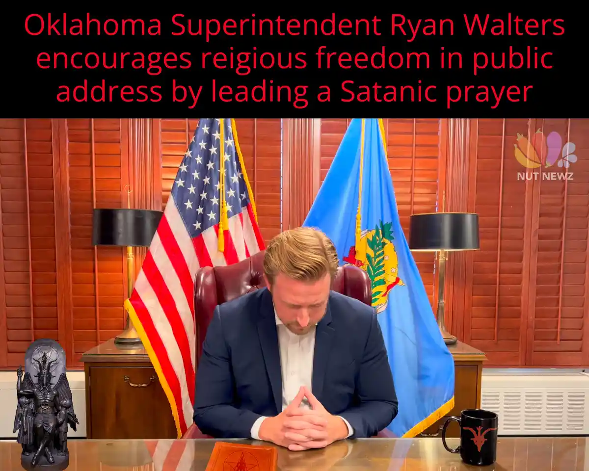 A man in a suit sits at a desk in an office with American and Oklahoma state flags behind him, head bowed in prayer…